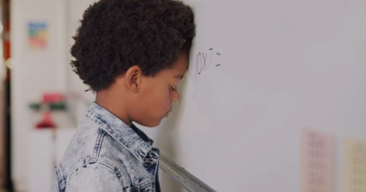 child with his head down on a whiteboard, looking discouraged